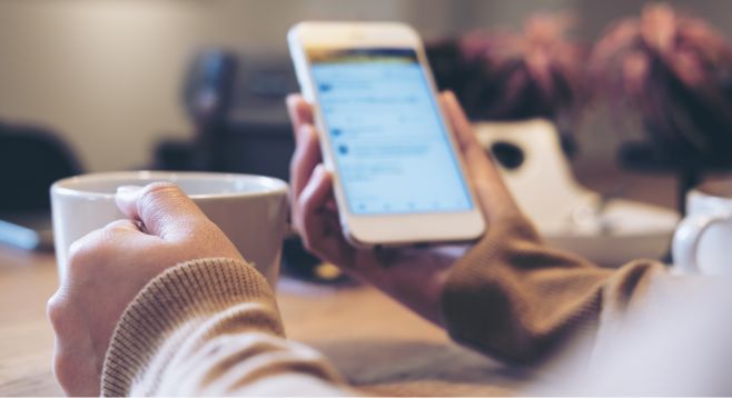 Closeup von Händen, die Kaffee halten und dabei aufs Handy schauen