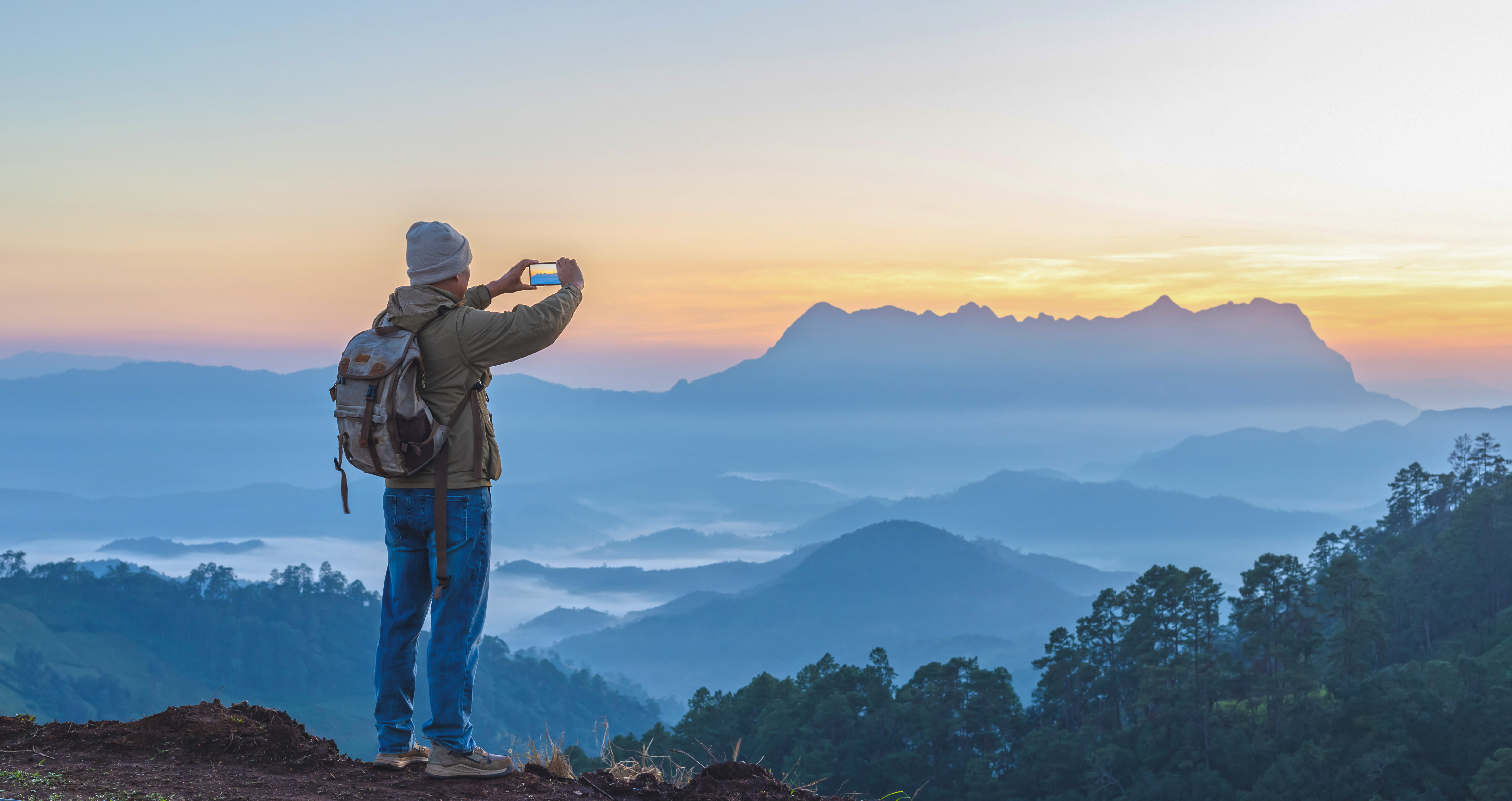 Male hiker with rucksack taking photos of a mountain landscape with his smartphone.