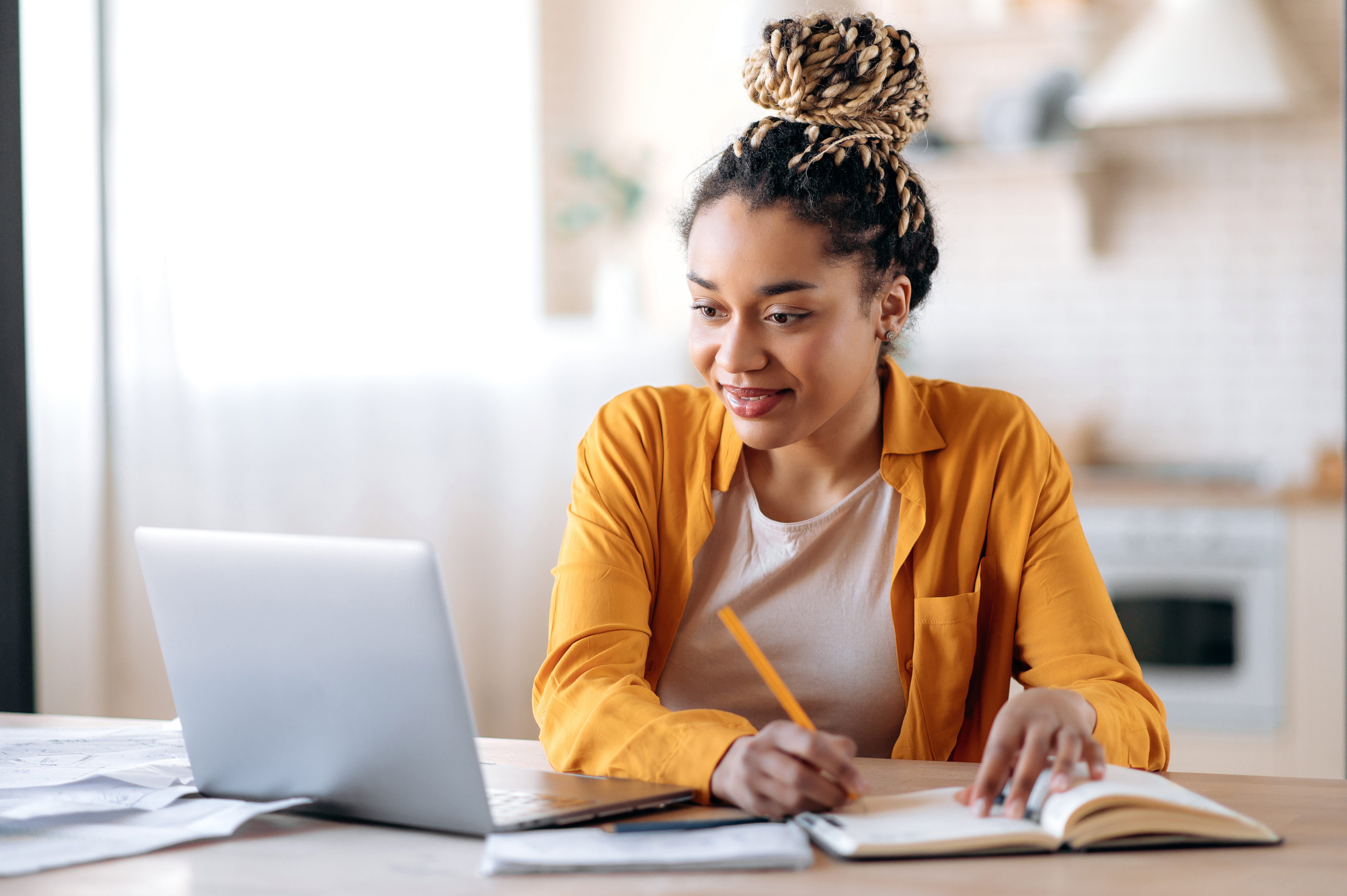 Konzentrierte afroamerikanische Studentin, die sich während des Online-Unterrichts Notizen auf einem Notizblock macht, E-Learning-Konzept