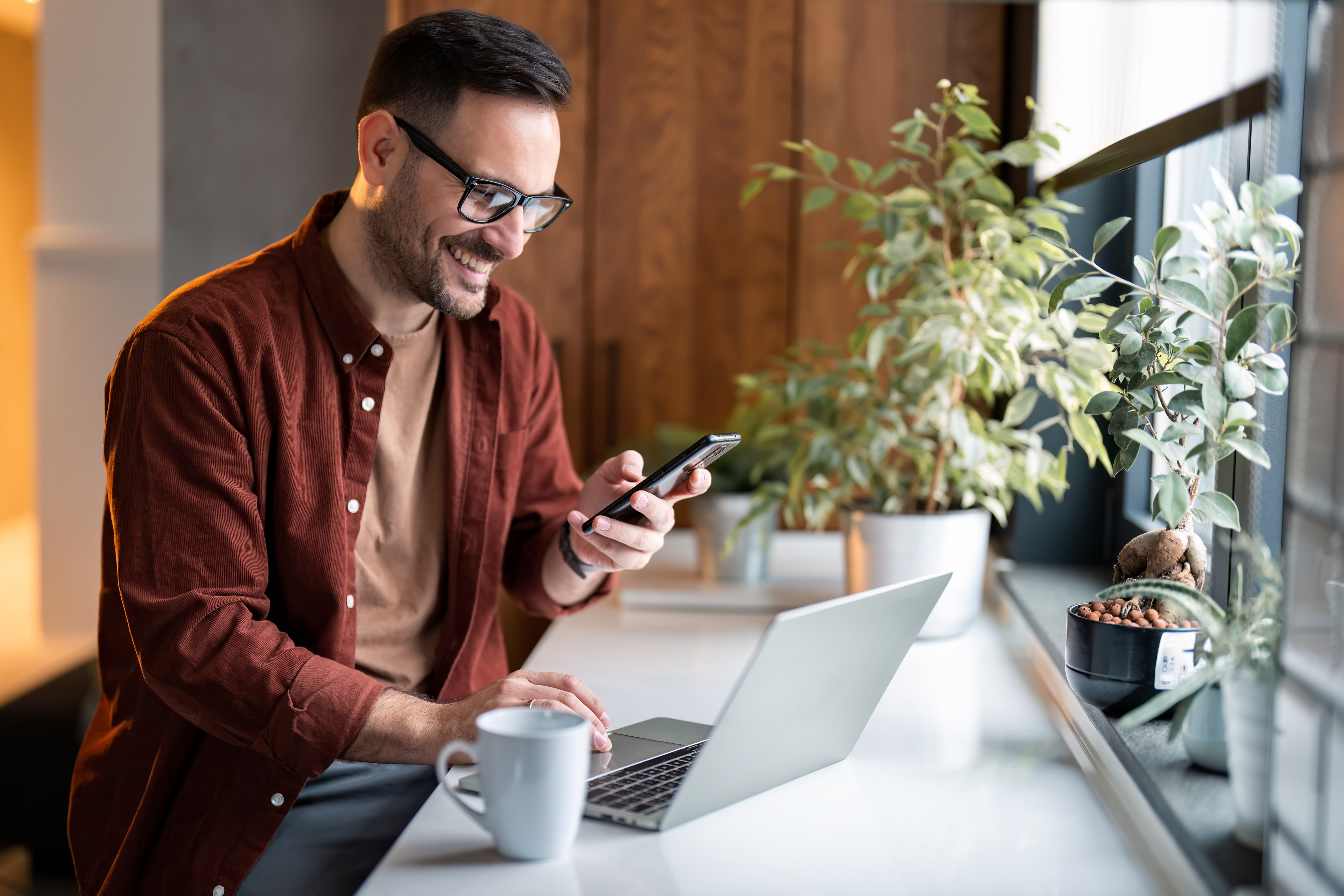 Satisfied modern millennial man in stylish leisurewear with smartphone and laptop