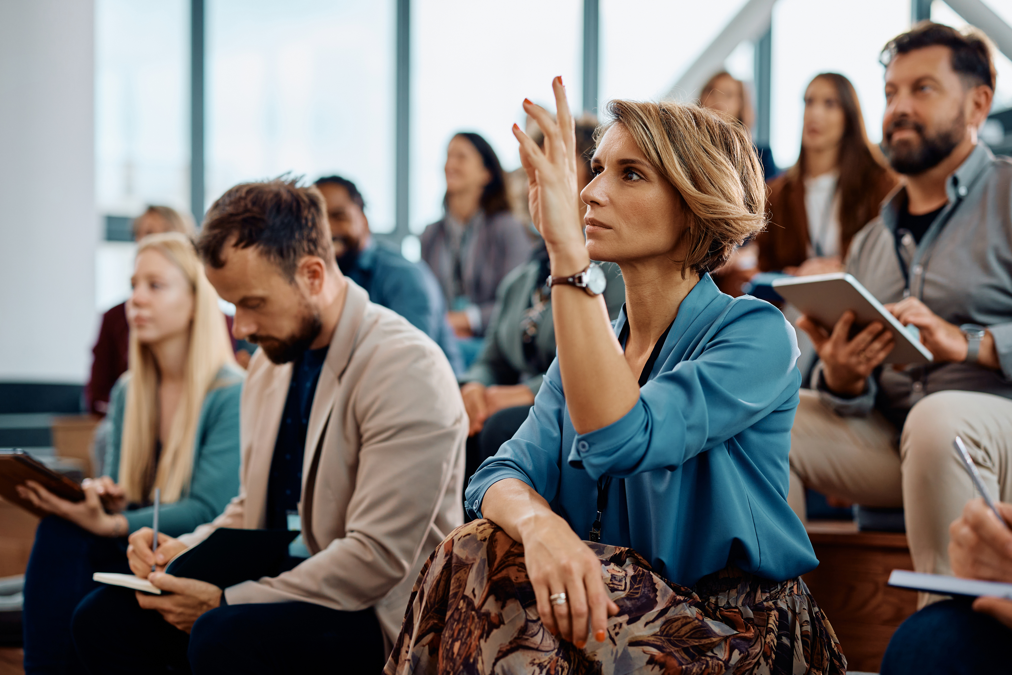 Geschäftsfrau, die die Hand hebt, um eine Frage zu stellen, die an einem Seminar im Konferenzsaal teilnimmt.