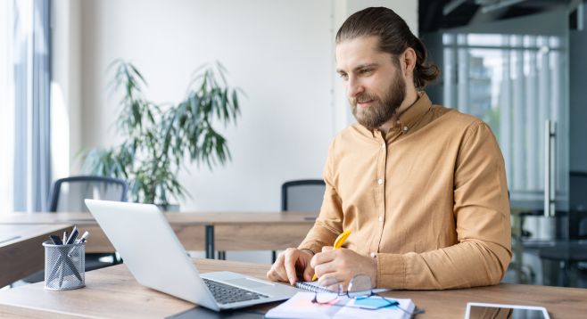 Mann sitzt am Laptop und macht sich Notizen